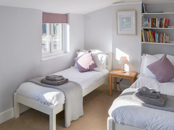 A bedroom with two single beds, a bedside table with a lamp, a bookshelf, and a window with a curtain.