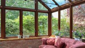 Ein Wintergarten mit Backsteinwand, einem roten, gemusterten Sofa und Blick auf Grünflächen.