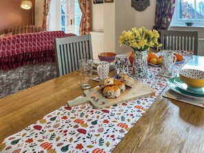 A dining table with a floral tablecloth, a vase of yellow flowers, and a bowl of oranges.