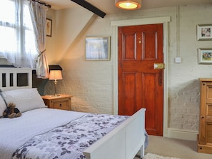 Une chambre à coucher avec un lit, une table de chevet, une lampe, une porte en bois et un petit meuble.