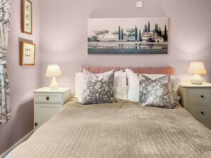 A bedroom with a bed, two bedside tables with lamps, a headboard, and a wall-mounted painting.