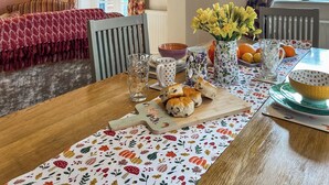 Ein Esstisch mit einer blumigen Tischdecke, einer Vase voller gelber Blumen und einer Schüssel Orangen.