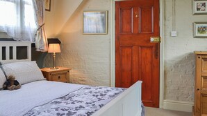 Ein Schlafzimmer mit einem Bett, einem Nachttisch, einer Lampe, einer Holztür und einem kleinen Schrank.