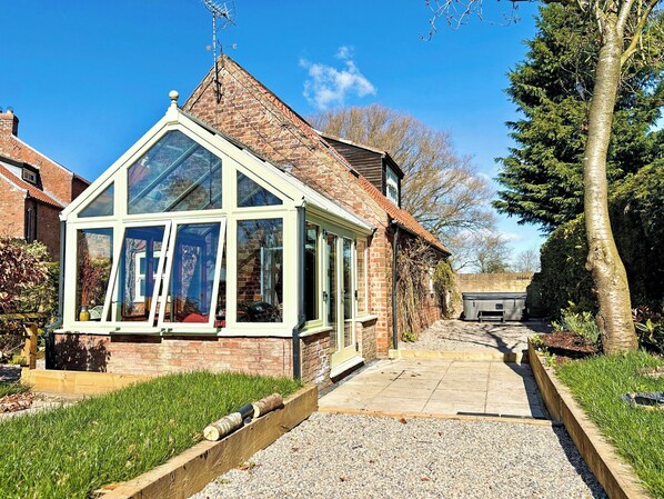 A conservatory with a brick exterior, a tiled roof, and a gravel pathway leading to it.