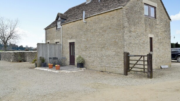 A stone building with a sloped roof, a wooden gate, and a gravel driveway.
