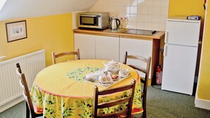 A small kitchen with a dining table set for two, a microwave, a kettle, and a refrigerator.