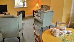 A cozy living room with a television, a fireplace, and a dining area with a table set for tea.