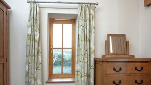 Une chambre avec une fenêtre, une commode en bois et une couvre-lit matelassé.