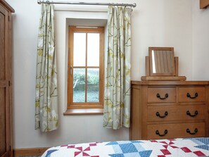 Un dormitorio con ventana, cómoda de madera y colcha acolchada.