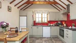Une cuisine avec des poutres en bois, un réfrigérateur blanc, un plan de travail rouge recouvert de carreaux et une table à manger en bois avec des chaises.