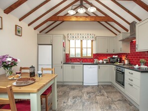 Una cocina con vigas de madera, un refrigerador blanco, un salpicadero de azulejos rojos y una mesa de comedor de madera con sillas.