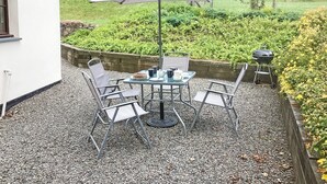 Une terrasse extérieure avec une table et des chaises, un barbecue et une vue sur le jardin.
