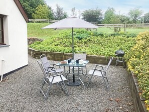 Un patio exterior con mesa y sillas, una parrilla y vistas a un jardín.