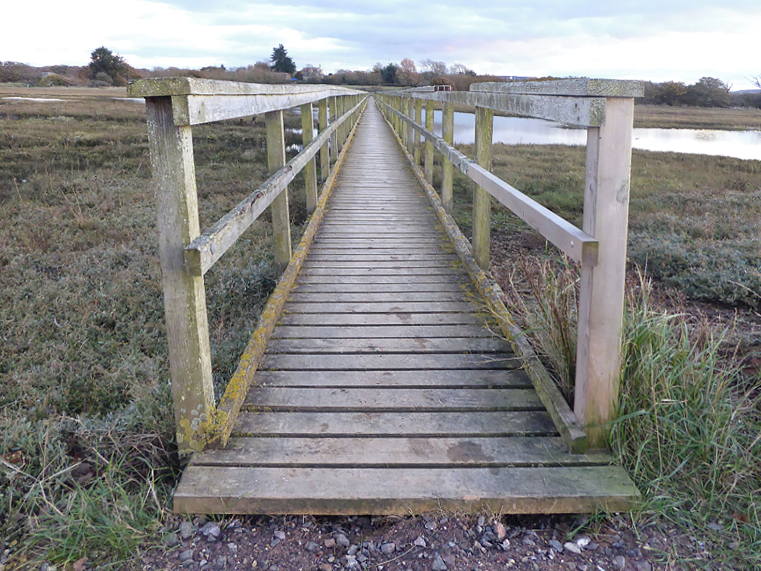 A wooden bridge with railings leading to a body of water.