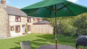 A stone house with a wooden deck, a round table with a green umbrella, and a barbecue grill. - 2 bedroom accommodation in Porchfield, near Newport (Porchfield, near Newport)