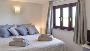 A neatly made bed with pillows and towels, a bedside lamp, and a window with curtains. - 2 bedroom accommodation in Porchfield, near Newport (Porchfield, near Newport)