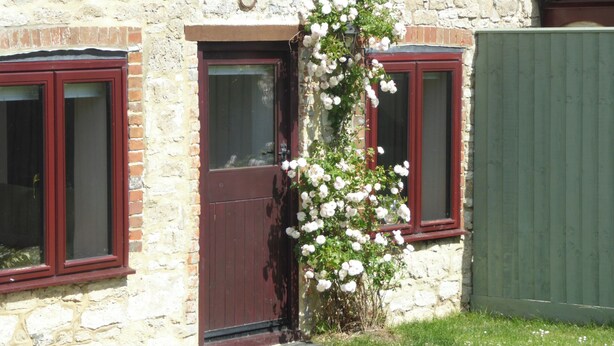 A stone building with a red door and windows, surrounded by a green fence. - 2 bedroom accommodation in Porchfield, near Newport (Porchfield, near Newport)