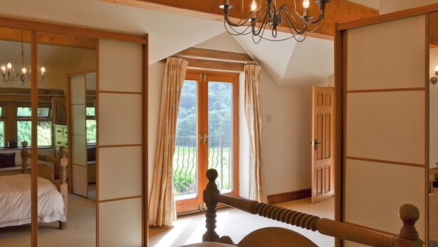 Une chambre dotée d’un grand lit, d’une tête de lit en bois, d’un lustre, d’une porte coulissante donnant sur un balcon et d’un miroir qui reflète la pièce.