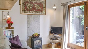 A cozy living room with a sofa, a small table with books, a television on a stand, and a decorative wall piece. - 1 bedroom accommodation in Bittaford, near Ivybridge (Bittaford, near Ivybridge)