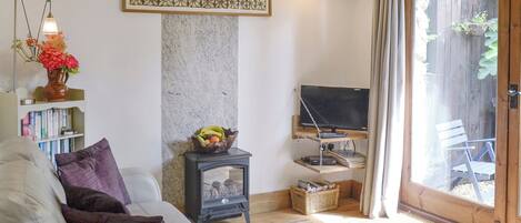 A cozy living room with a sofa, a small table with books, a television on a stand, and a decorative wall piece.