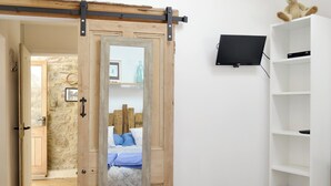 A bedroom with a bed, a TV mounted on the wall, a wooden door, and a white shelf. - 1 bedroom accommodation in Bittaford, near Ivybridge (Bittaford, near Ivybridge)