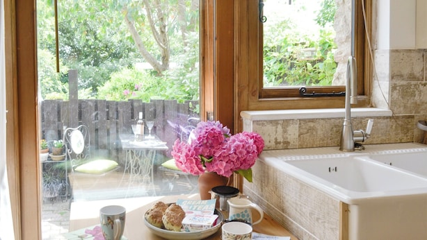A kitchen with a large window, a sink, and a table with a vase of flowers, a plate of scones, and a mug. - 1 bedroom accommodation in Bittaford, near Ivybridge (Bittaford, near Ivybridge)