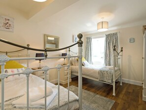A bedroom with two beds, a mirror, a bedside table with a lamp, and a window with curtains.