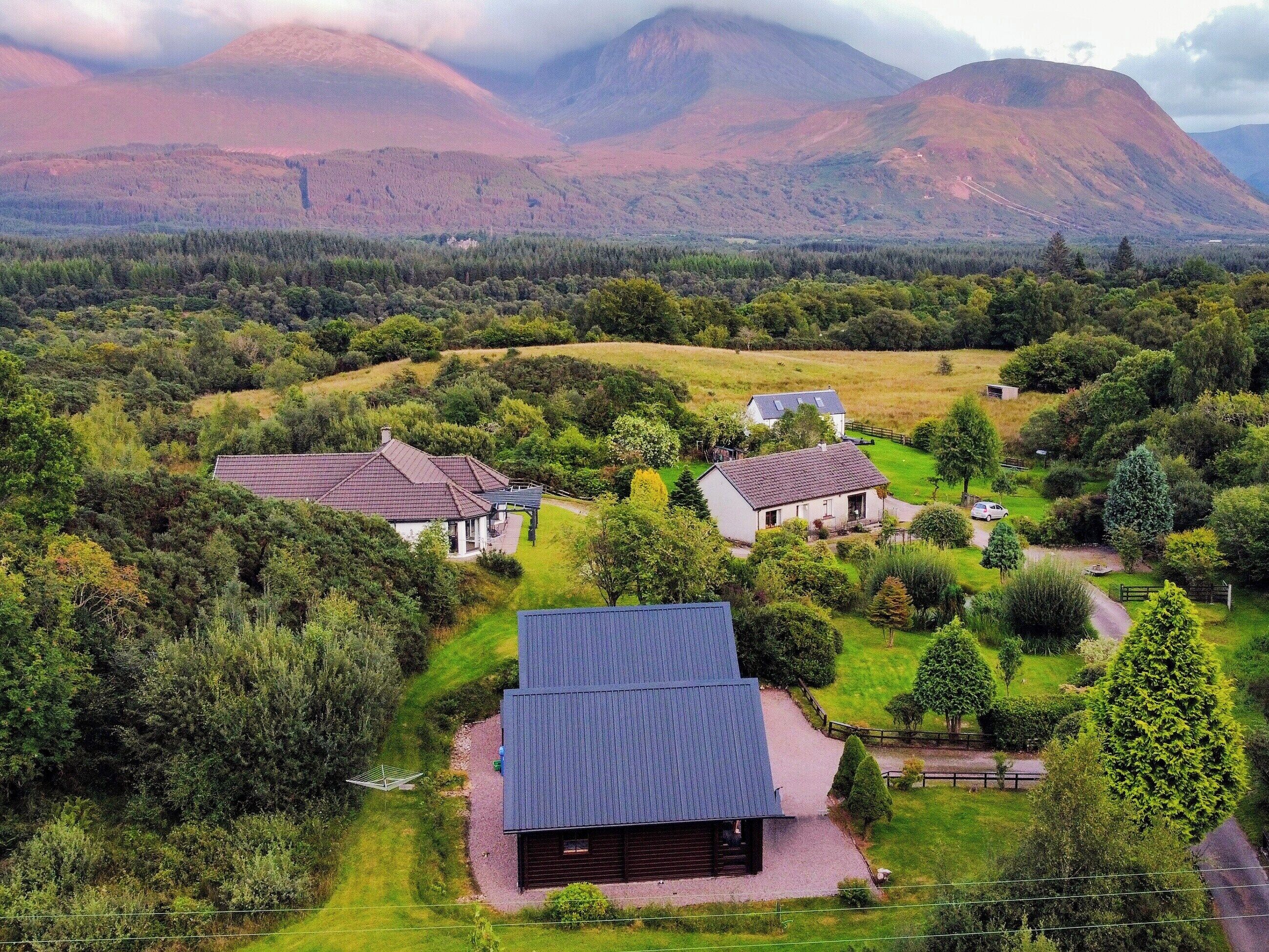 A rural landscape with houses surrounded by greenery and mountains in the background.