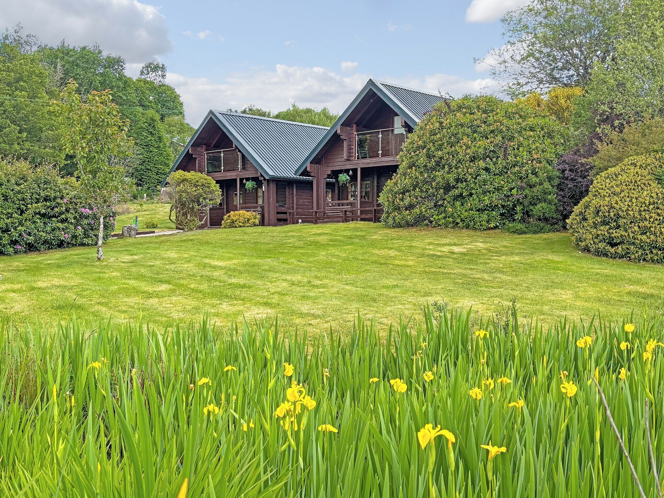 Une cabane en bois à deux étages, dotée d’un toit en pente, entourée d’une végétation luxuriante et d’une pelouse bien entretenue.