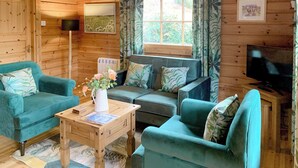 Interior acogedor de una cabaña con sofá, una mesita de centro, televisor y ventana con cortinas.