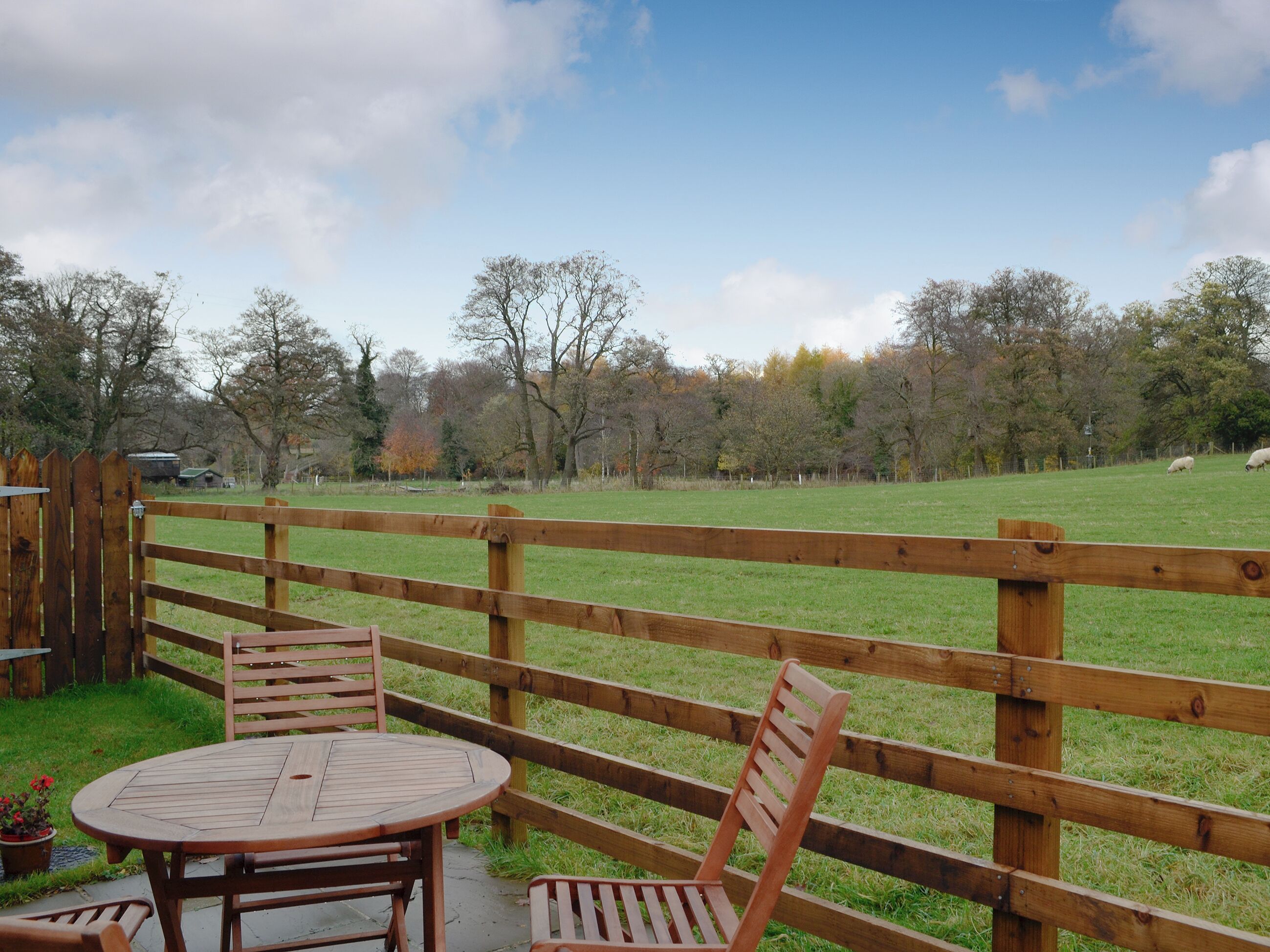 A wooden fence with a table and chairs in a grassy area.