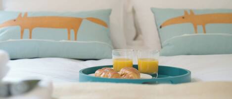 A bed with light blue pillows featuring animal prints, a teal tray with croissants and orange juice, and a white headboard.