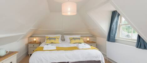 A bedroom with a bed, bedside tables, a hanging light fixture, a window with curtains, and a ceiling light.