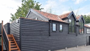 A modern building with a dark exterior, a red-tiled roof, and a wooden staircase leading to a door. - 2 bedroom accommodation in Beccles, near Gillingham (Beccles, near Gillingham)