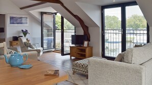 A spacious living area with a high ceiling, wooden beams, a sofa, a coffee table with a teapot, a TV stand, and large windows offering a view of the outside. - 2 bedroom accommodation in Beccles, near Gillingham (Beccles, near Gillingham)