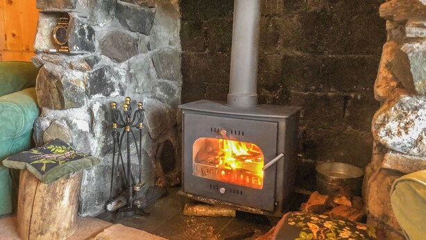 En stenkamin med en vedeldad kamin, ett litet bord med en dekorativ detalj och en vadderad bänk.