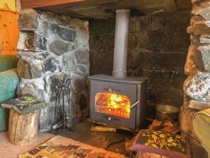 A stone fireplace with a wood-burning stove, a small table with a decorative item, and a cushioned bench. - 3 bedroom accommodation in Invergarry, Tomdoun (Invergarry, Tomdoun)