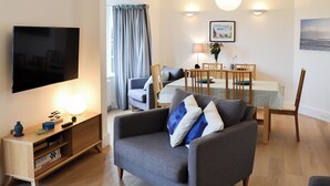 Un salon moderne doté d’un téléviseur à écran plat, d’un canapé, d’une table à manger en bois avec des chaises et d’une grande fenêtre agrémentée de rideaux.