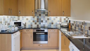 A modern kitchen with wooden cabinets, a stainless steel range hood, a microwave, an oven, a dishwasher, and a sink with a faucet. - 2 bedroom accommodation in East Charleton, near Kingsbridge (East Charleton, near Kingsbridge)