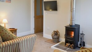 A living room with a sofa, a fireplace, a TV mounted on the wall, and a door leading to another room. - 2 bedroom accommodation in East Charleton, near Kingsbridge (East Charleton, near Kingsbridge)