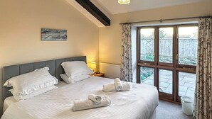 A neatly made bed with pillows and towels, a bedside lamp, a window with curtains, and a painting on the wall. - 2 bedroom accommodation in East Charleton, near Kingsbridge (East Charleton, near Kingsbridge)
