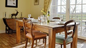 A dining room with a wooden table set for four, chairs, a vase with flowers, and framed pictures on the wall. - Osprey Cottage - UZQ (Meigle)