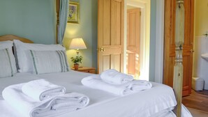 A neatly made bed with white linens and towels, a bedside lamp, and a wooden door in the background. - Osprey Cottage - UZQ (Meigle)