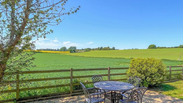 A patio with a table and chairs, a wooden fence, and a view of a green field. - Osprey Cottage - UZQ (Meigle)