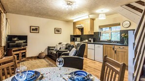 A living room with a TV, sofa, and dining table set with blue plates and wine glasses. - 2 bedroom accommodation in Ledbury (Ledbury)