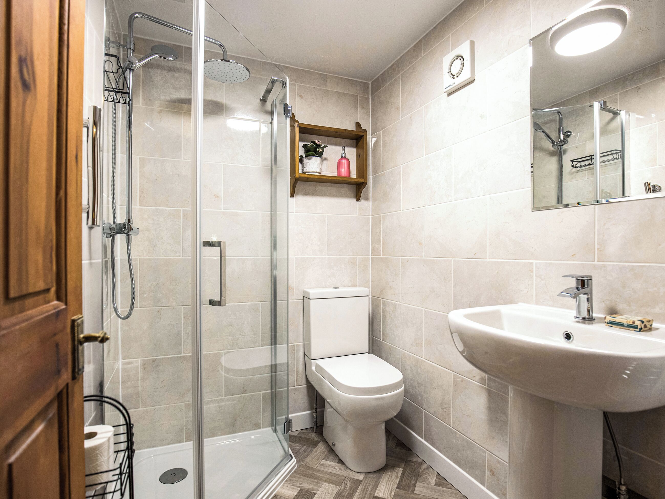 A bathroom with a glass shower enclosure, a toilet, a sink, and a mirror.