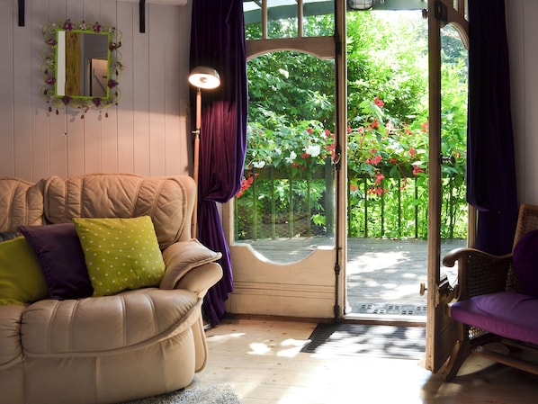 A cozy room with a cushioned sofa, a wooden door leading to a garden, and a wicker chair.