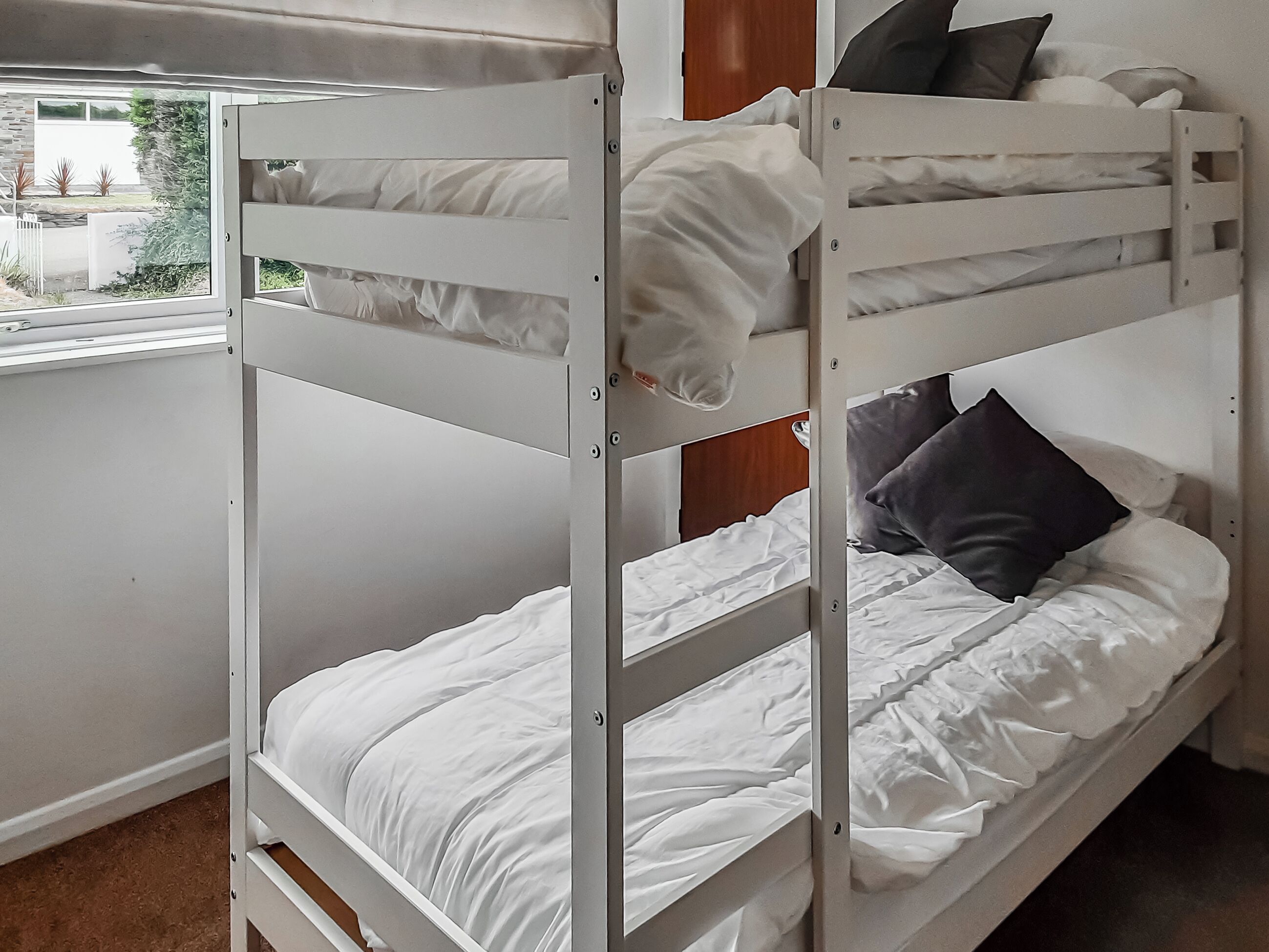 Una cama litera con ropa de cama blanca y vista a la ventana.
