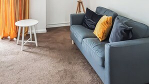 Een woonkamer met een blauwe bank, een witte tafel en een vloerlamp.