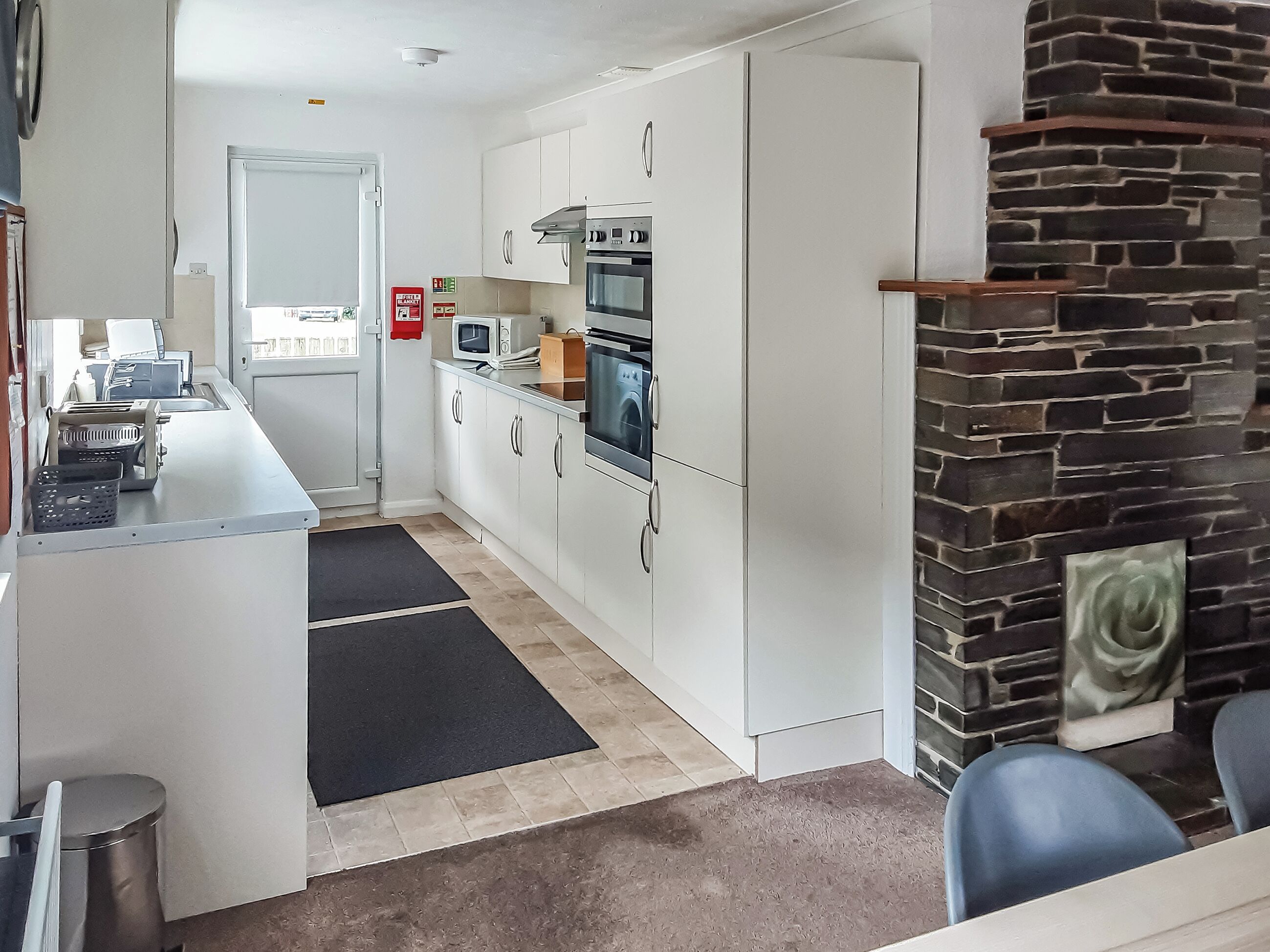 A compact kitchen with white cabinets, a microwave, an oven, and a stone fireplace.